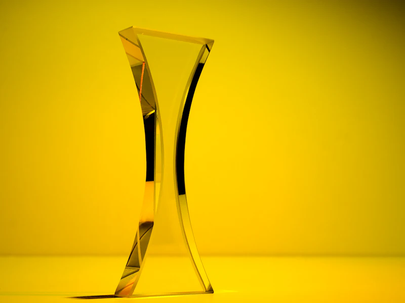 A curved clear glass award standing on a yellow background